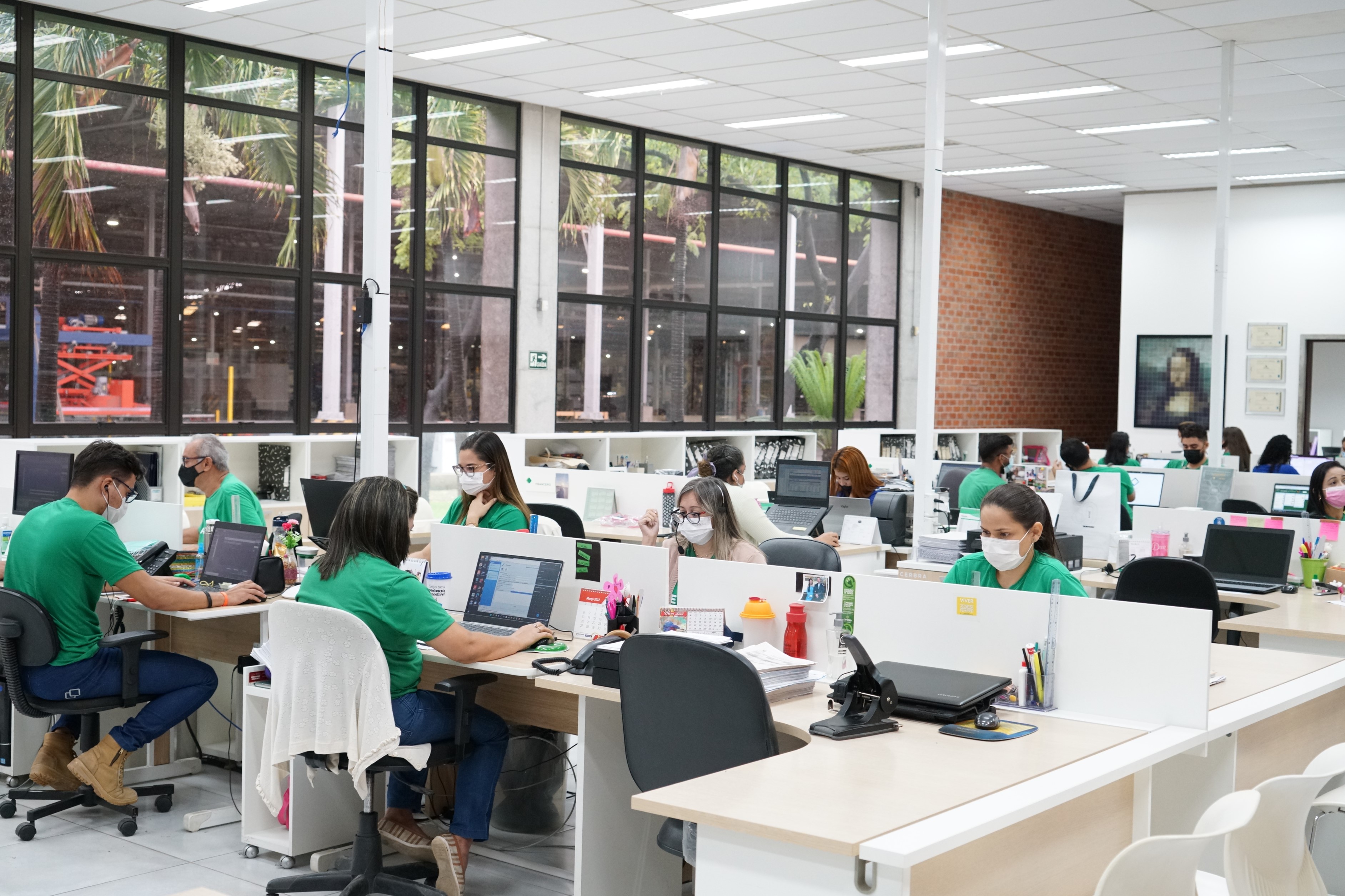 Foto de ambiente com inúmeros funcionários trabalhando em computadores