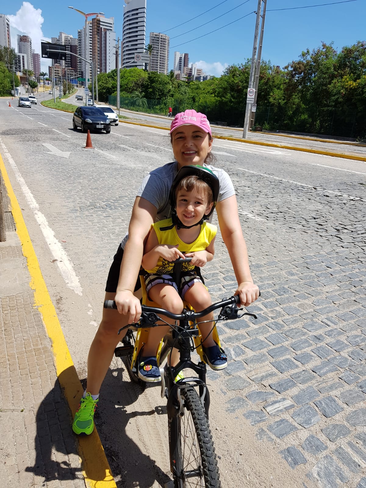 imagem de raffaella e bernardo com traje esportivo em uma bicicleta, ele está em um assento infantil entre os braços de sua mãe sorrindo