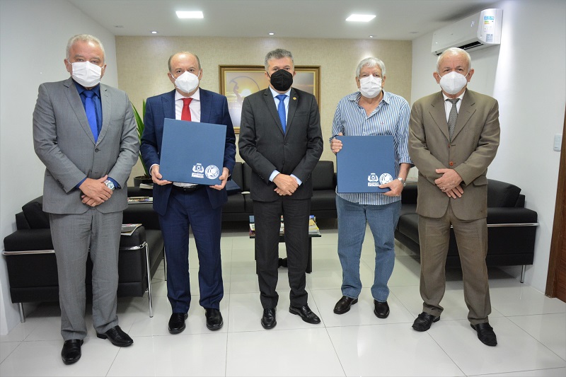 imagem de cinco homens brancos de meia idade quatro deles de terno, exceto o desembargador jefferson quesado que veste jeans e blusa social, todos estão em uma sala com paredes brancas, exceto pela parede atrás deles que é amarela e há também três sofás pretos e uma mesinha de centro atrás dos homens