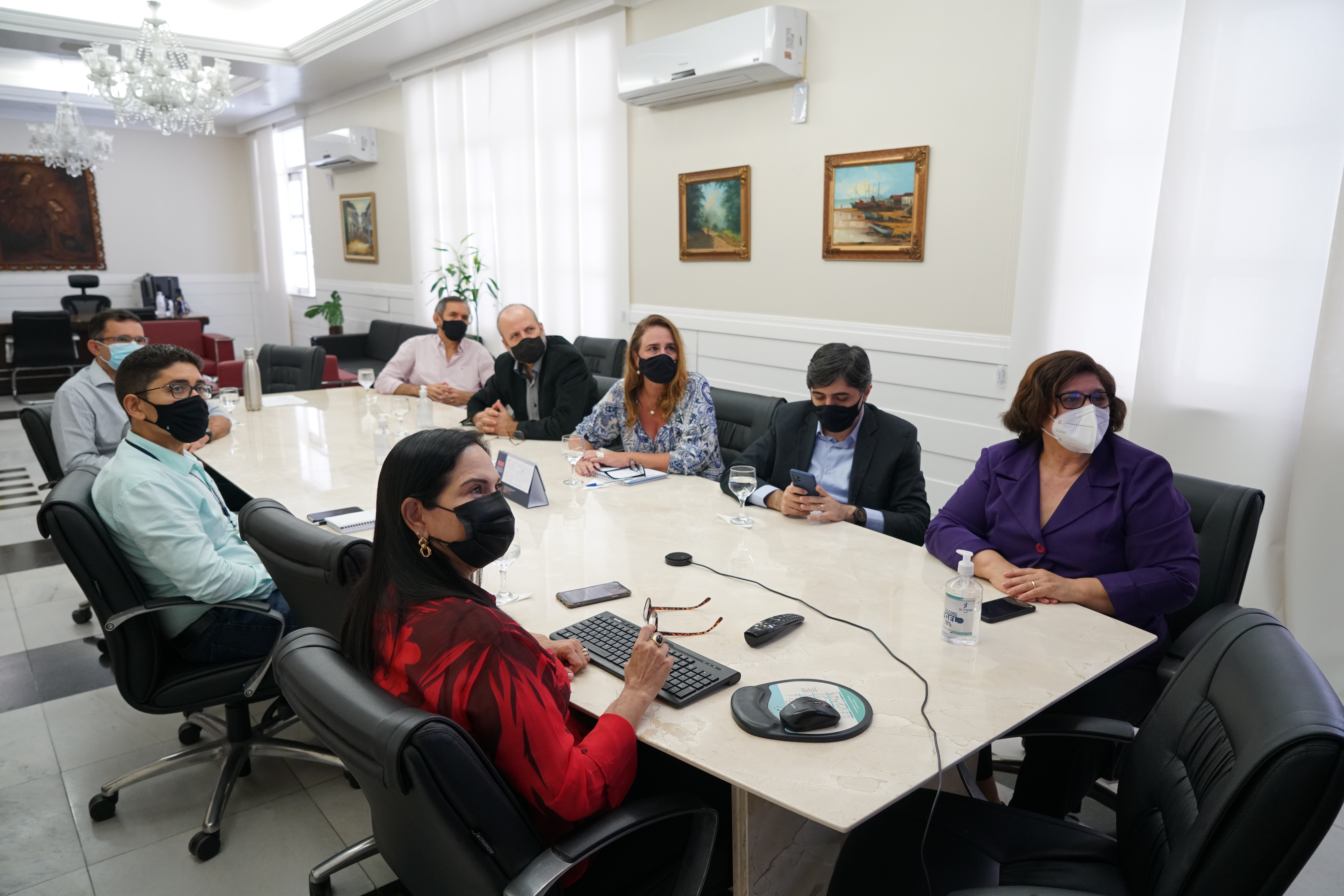 Foto da reunião com a presidente do Tribunal, diretora geral, dentre outros servidores. Estão sentados assistindo à apresentação do relatório por slides.