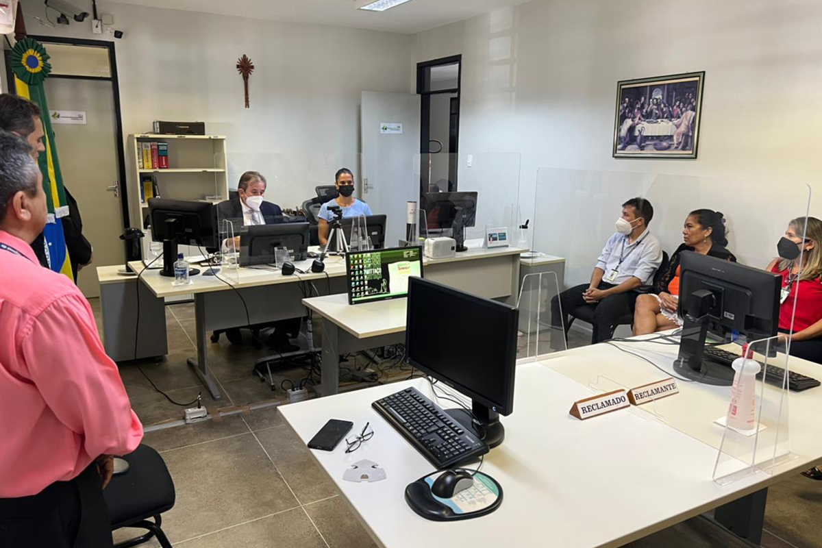 Foto da sala de audiência. Estão presentes o corregedor, juíza, servidores e estagiários