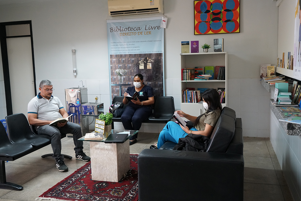 Foto de três pessoas sentadas lendo livros em frente à biblioteca livre