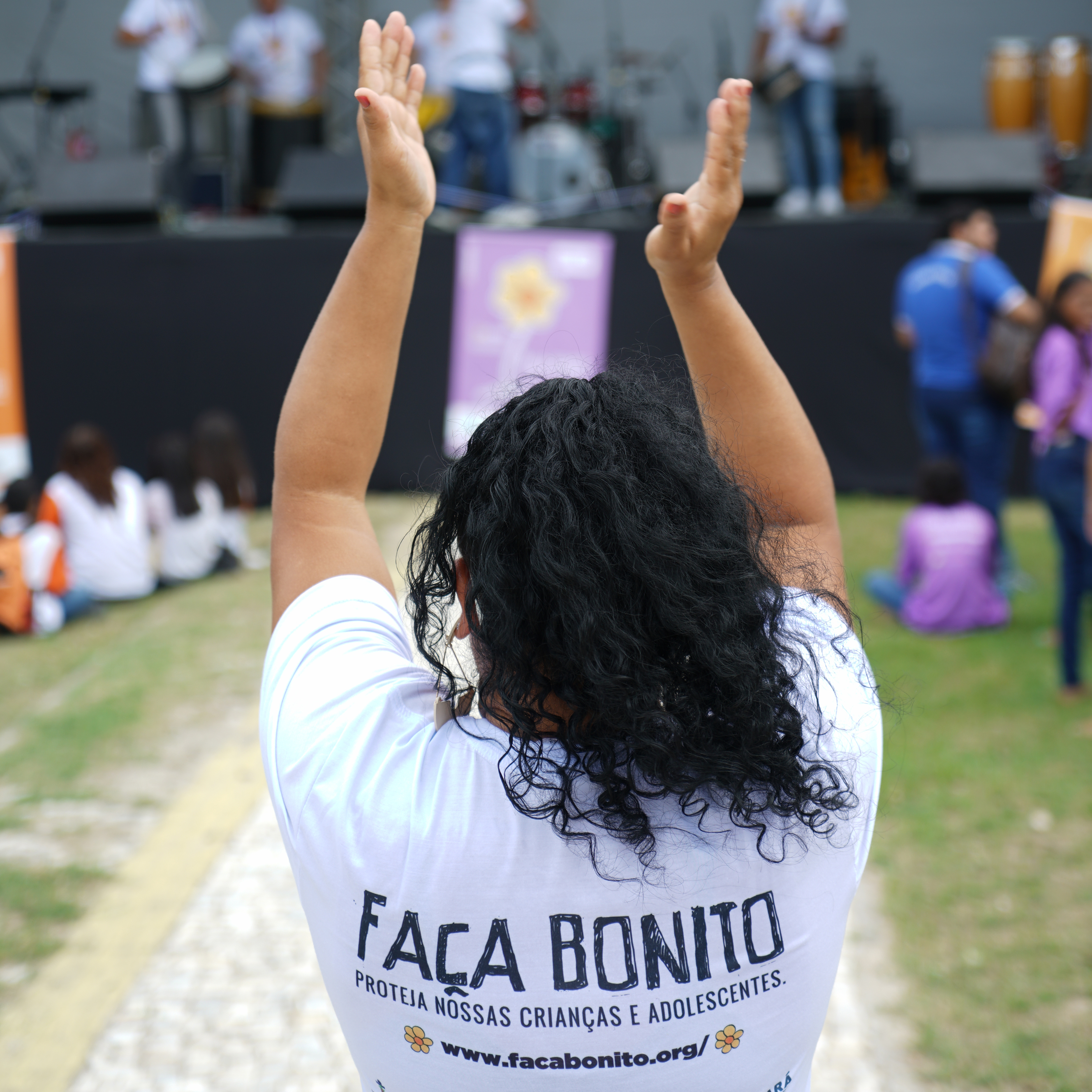 Jovem de costas bate palmas para a apresentação musical que ocorre no palco