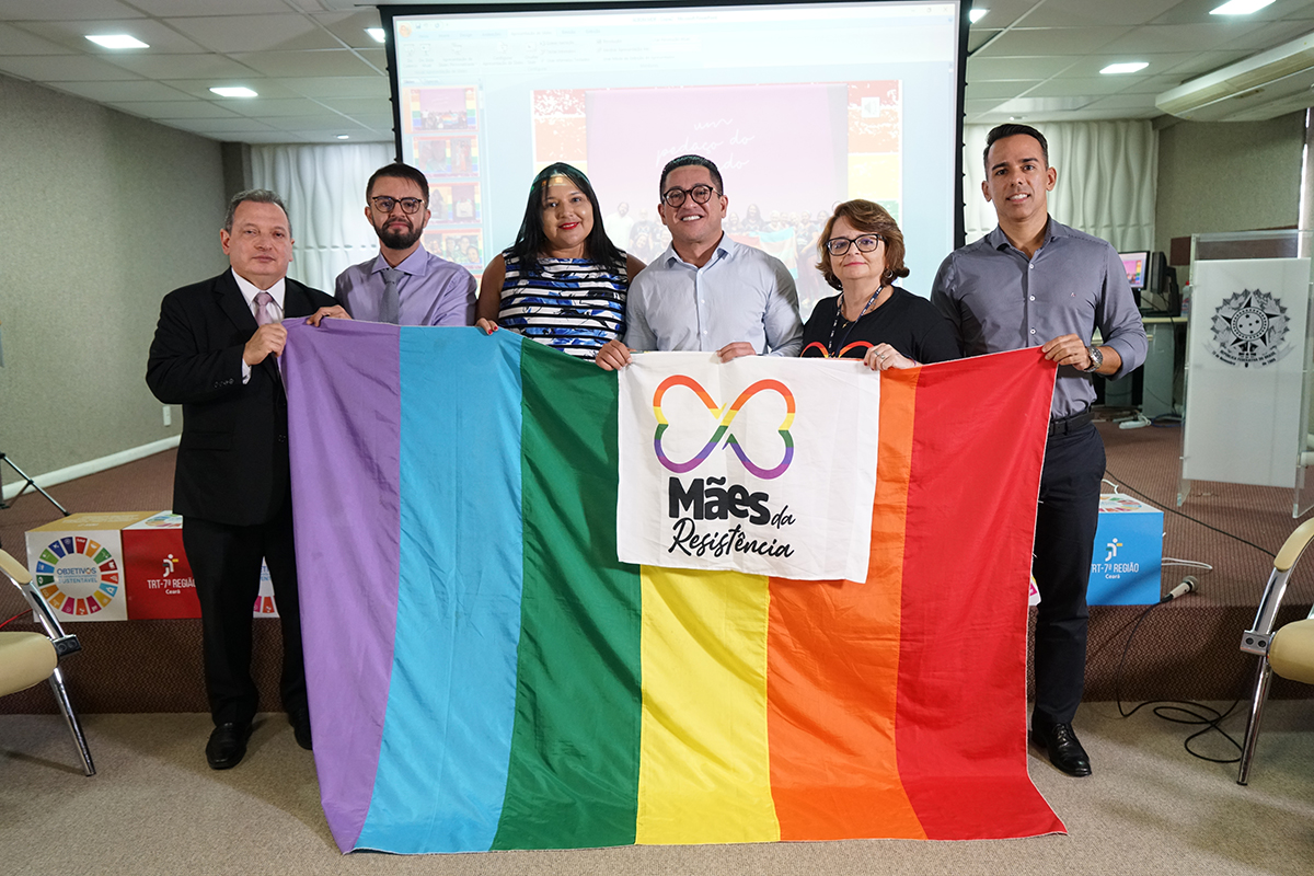 Foto dos palestrantes e presidente do TRT-CE segurando uma bandeira do arcoíris. Estão no auditório da Escola Judicial