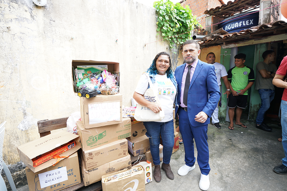 caixas de papelão com brinquedos e livros para doação, juiz de terno e gravata e a Lenice, dona da biblioteca