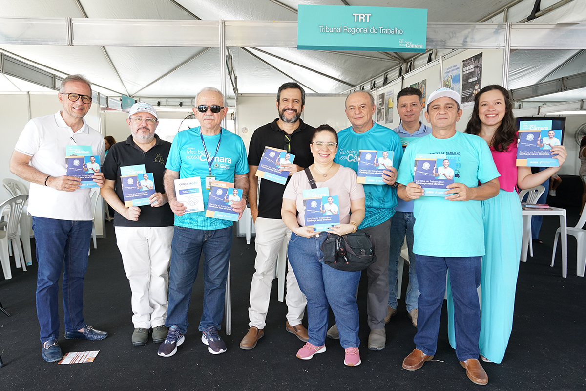 Grupo de pessoas em pé no estande do TRT7 com a cartilha do trabalhador