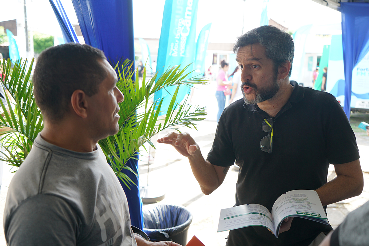 um homem segura cartilha e gesticula em direção a um trabalhador