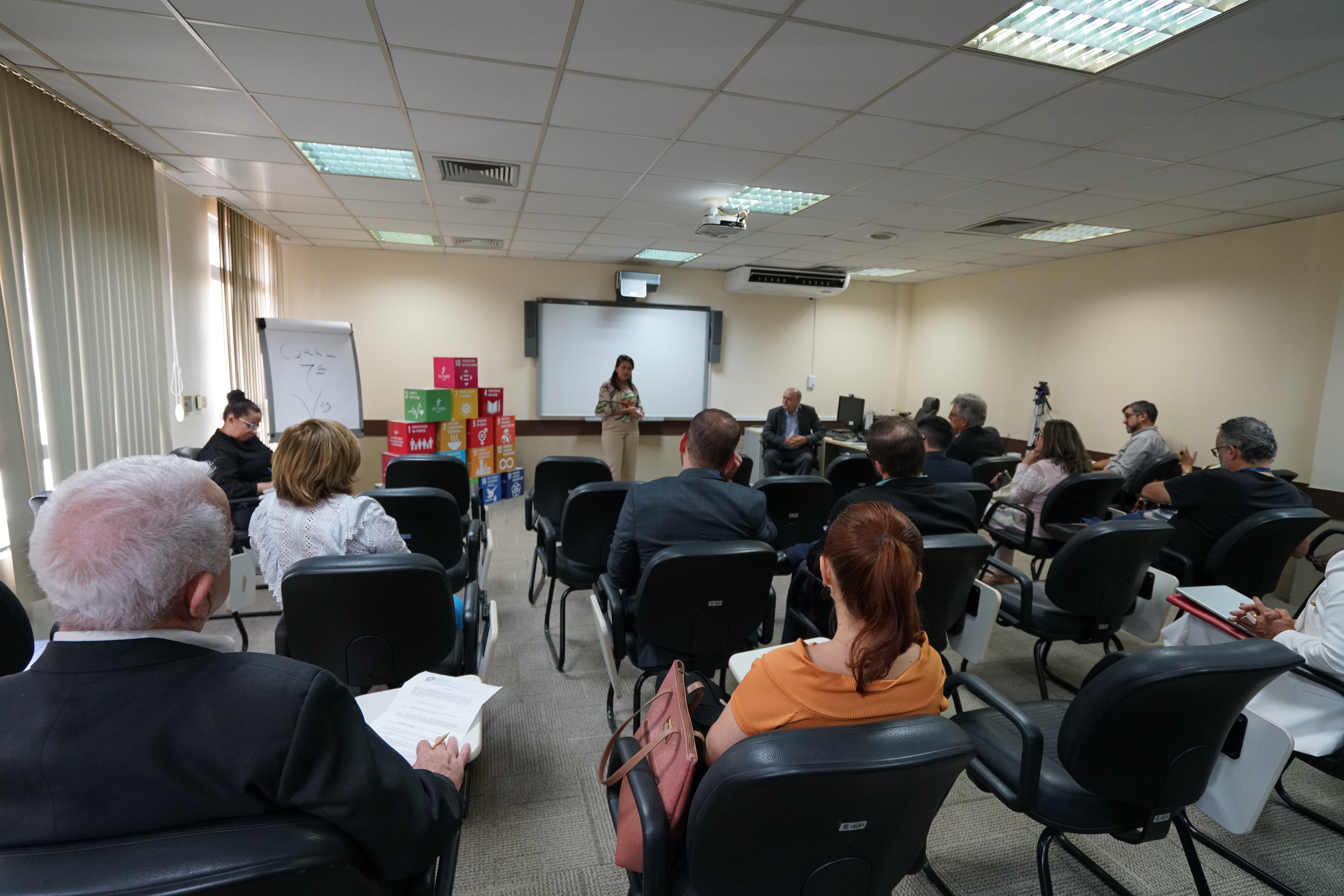 Foto da reunião onde a chefe de cerimonial, Carmem Frota, e o desembargador do TRT-7, José Antônio Parente, estão falando para o público. Nesse momento, ela está em pé, e ele, sentado ao lado dela.