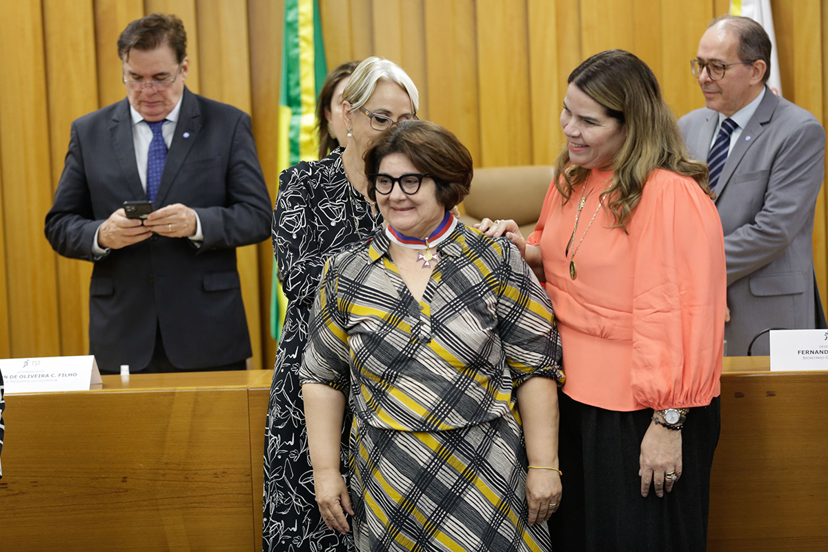 Mulher coloca medalha no pescoço de outra mulher