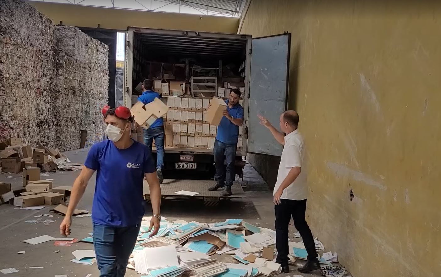 Foto de homens trabalhando retirando caixas de papelão para colocar no galpão. Há três trabalhadores terceirizados usando farda azul e um servidor do TRT vestindo camisa branca e calça preta