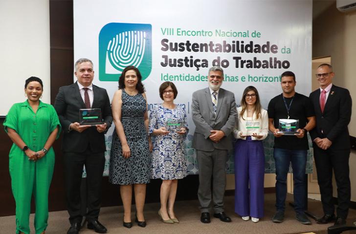 Fotografia em ambiente fechado que reúne oito pessoas em pé, entre homens e mulheres