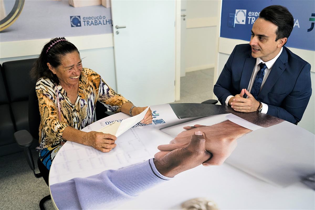 Mulher sentada na mesa com o juiz olha o papel do alvará e sorri