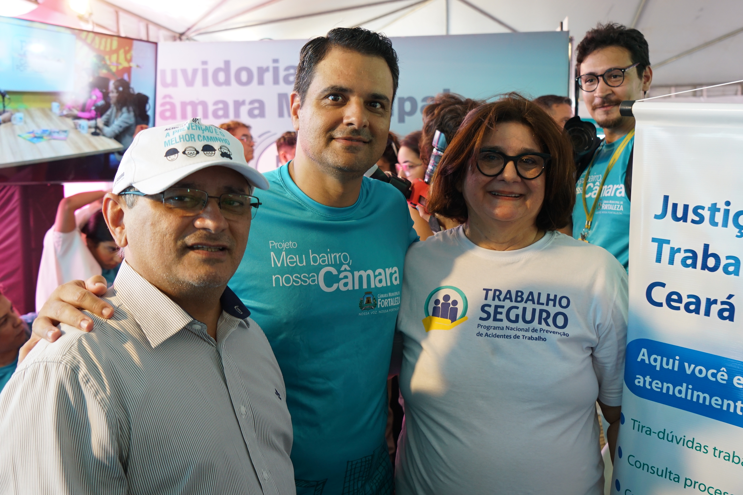 Foto dos Gestores Regionais do Programa Trabalho Seguro, magistrado Raimundo Neto e desa. Regina Gláucia ladeando o prefeito em exercício Gardel Rolim (centro). Eles estão em pé, sorrindo e ao lado do banner da Justiça do Trabalho