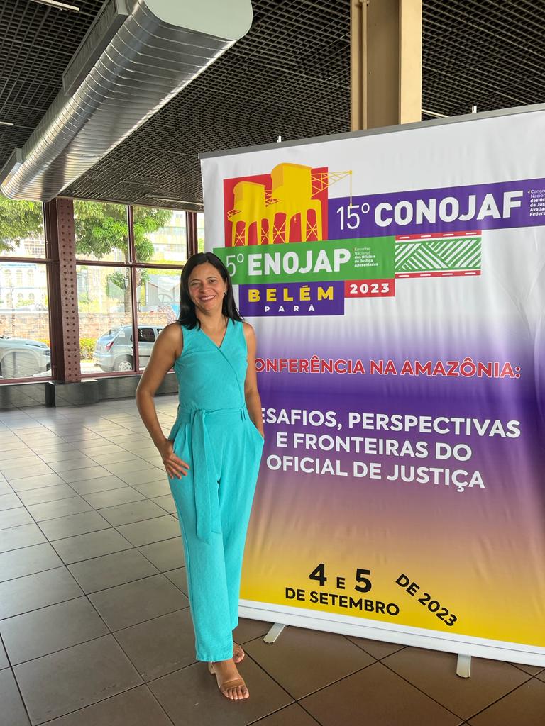 Sandra Mara no 15º Congresso Nacional dos Oficiais de Justiça Avaliadores Federais em 2023. Ela está em pé, numa roupa azul e atrás dela tem um banner com o nome do congresso