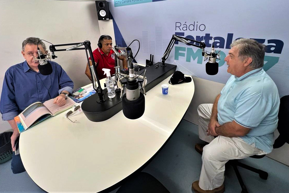 três homens sentados numa mesa com microfones em um estúdio móvel de rádio