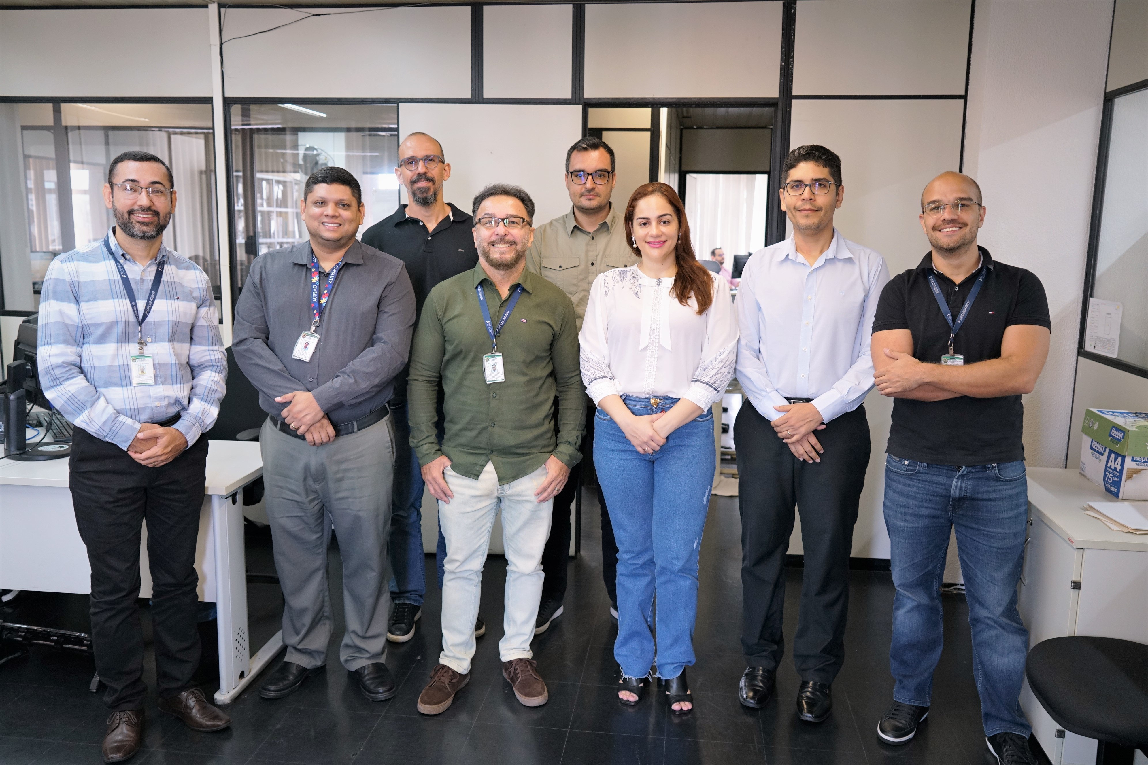 Foto dos participantes do curso na secretaria de orçamento e finanças. Os servidores do TRT do Ceará e do Amazonas estão em pé, sorridentes e alguns usam crachá. Há 7 homens e uma mulher.