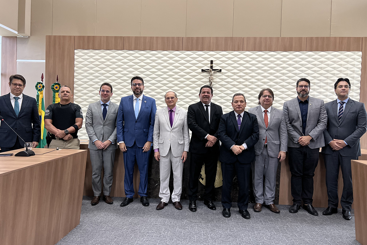 Dez homens de paletó em pé na frente de uma mesa de auditório