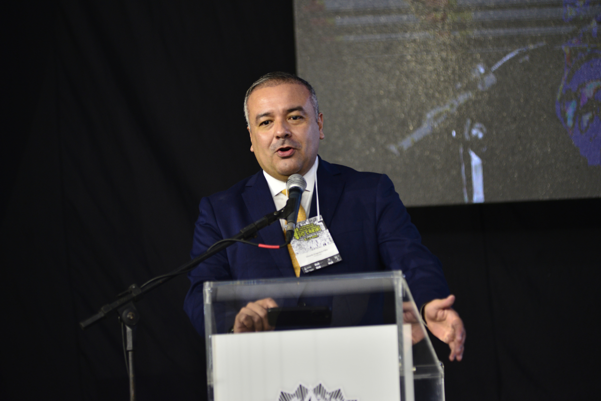 homem de paletó fala ao microfone na tribuna do evento