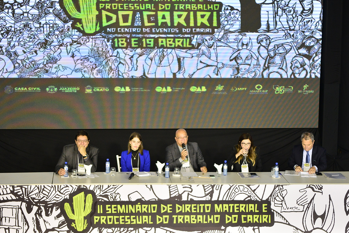 mesa do evento com 5 pessoas sentadas, painel do evento atrás