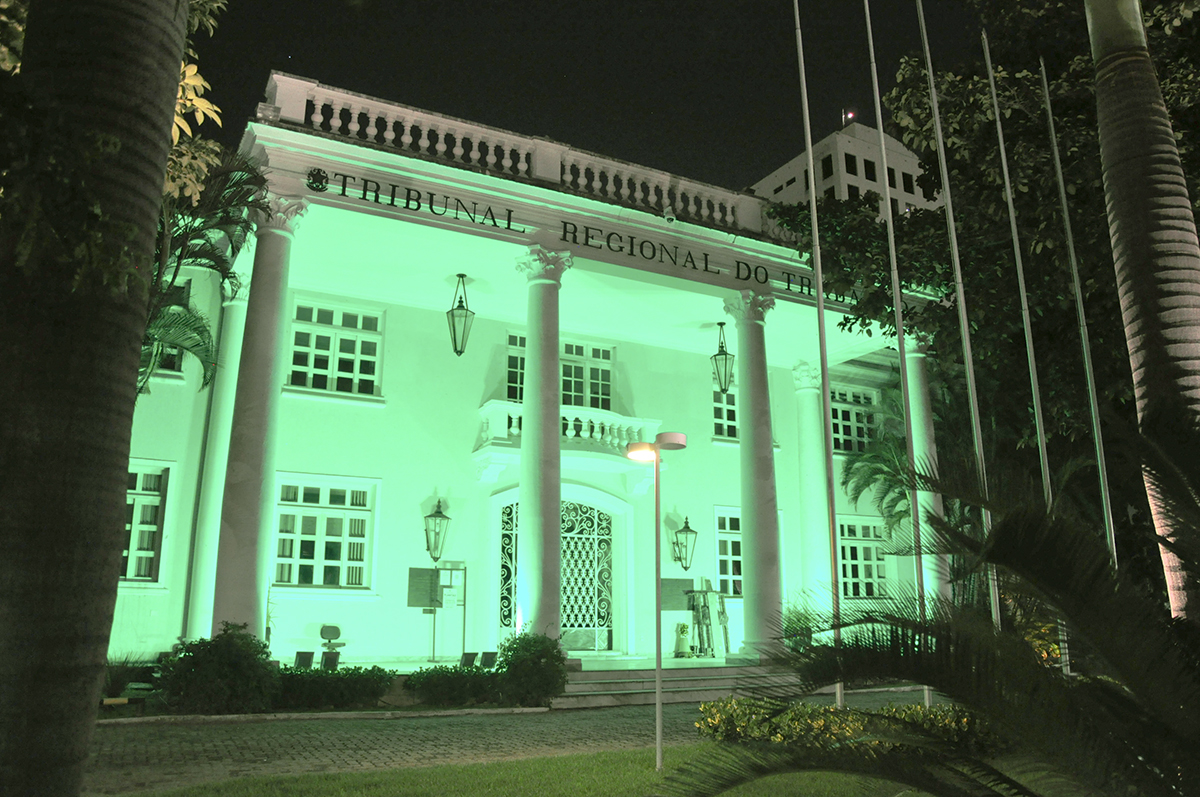 Foto do prédio sede do TRT-7 iluminado, à noite, na cor verde. A fachada é imponente, na cor branca e foi inspirada no filme "E o vento levou"