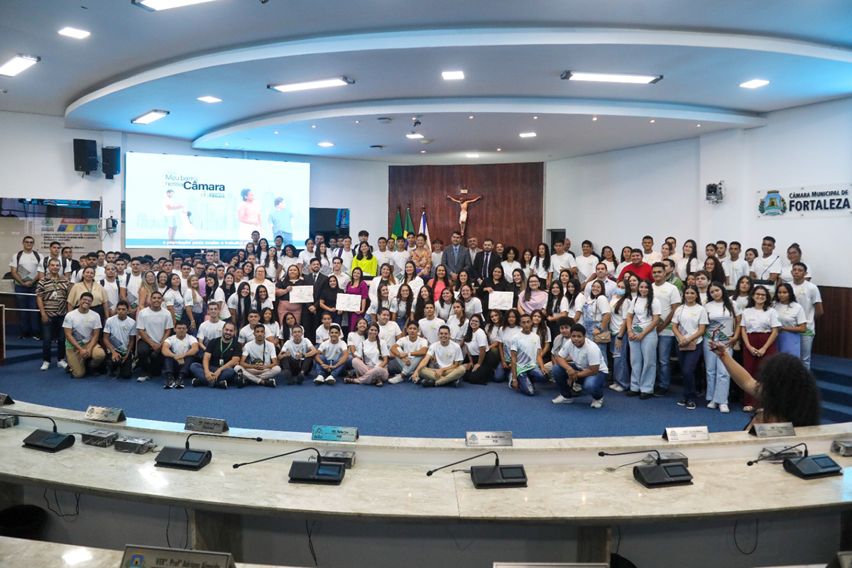 plenário da Câmara repleto de pessoas, maioria jovens fardados, posam para foto, há um telão atrás e um jesus crucificado