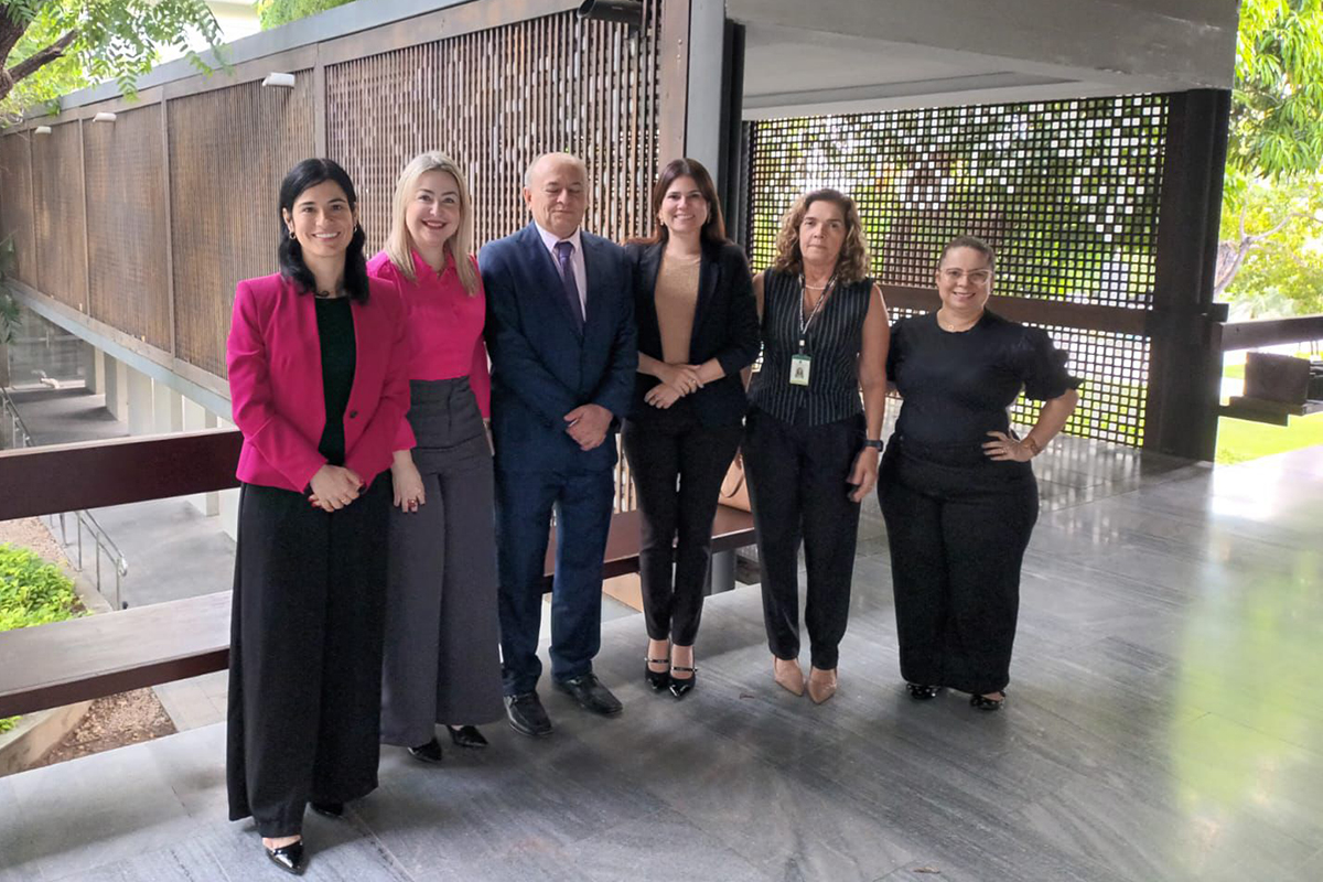 Cinco mulheres e um homem em pé posam para foto em um jardim arborizado