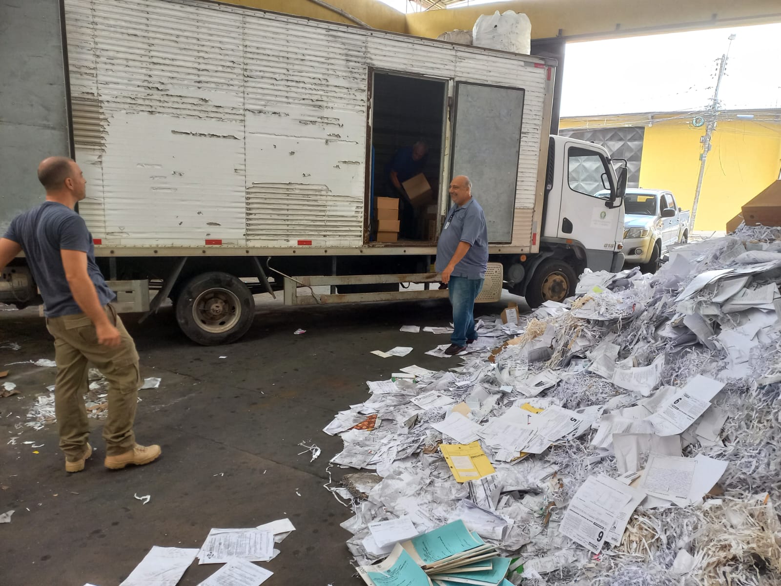 Caminhão com baú aberto recebendo carregamento de pilhas de papel