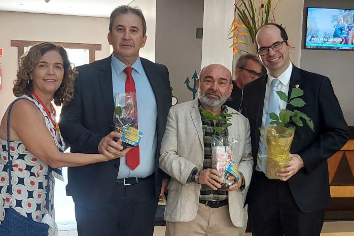 uma mulher e três homens de paletó seguram muda de planta