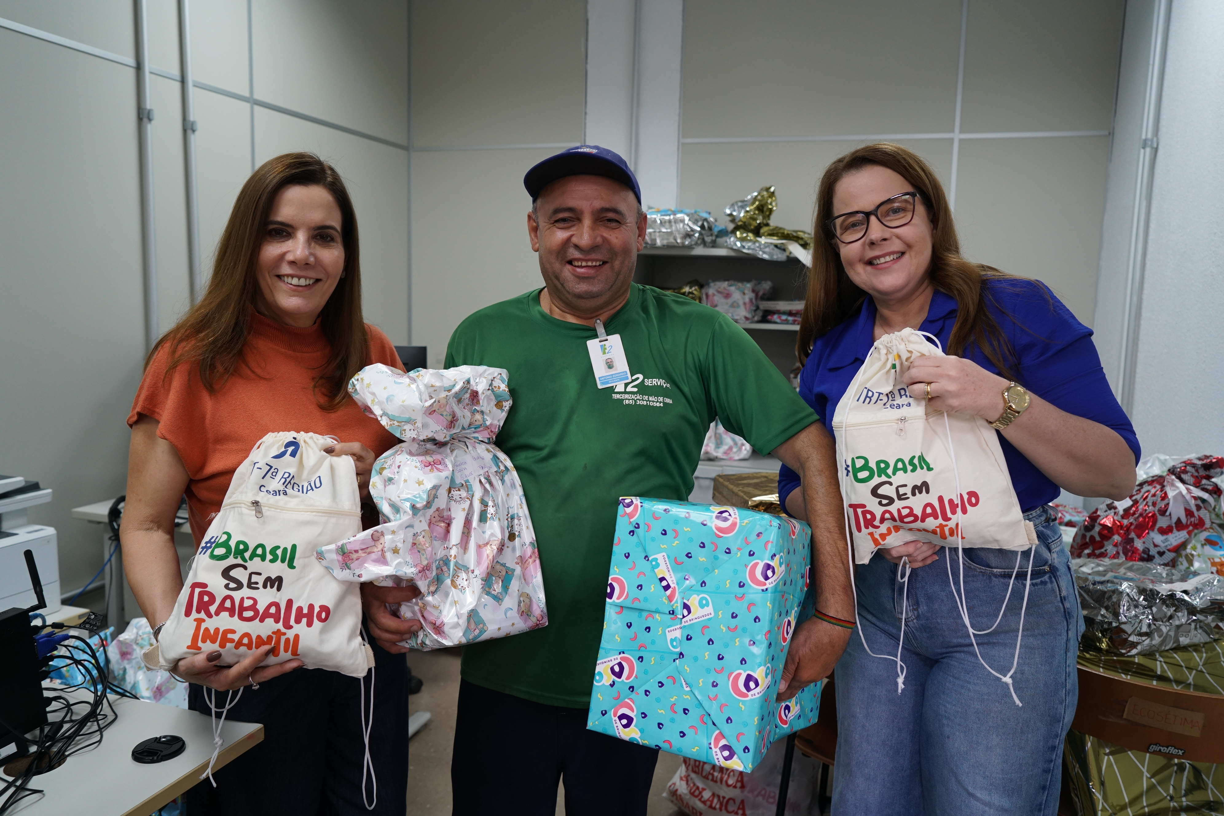 Neuzinha Sucupira e Karina Bessa fazendo entrega aos terceirizados do TRT-CE. Eles estão posando para foto, segurando presentes e mochilas do Programa de Combate ao Trabalho Infantial e sorrindo para a foto.