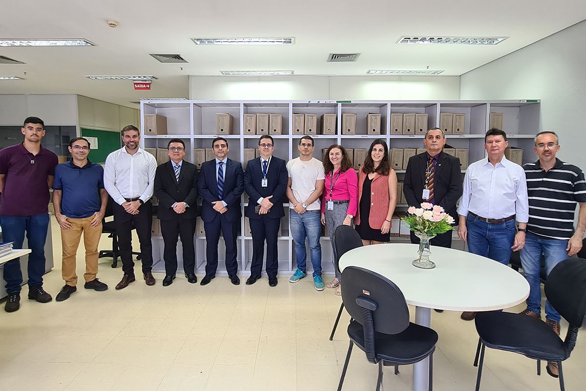  Doze pessoas em pé posam pra foto na secretaria da vara, com estantes de processos ao fundo e uma mesa com jarro de flores à frente