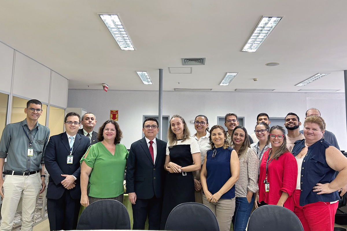 pessoas em pé posam pra foto no centro da secretaria da vara, com estantes de processos ao fundo