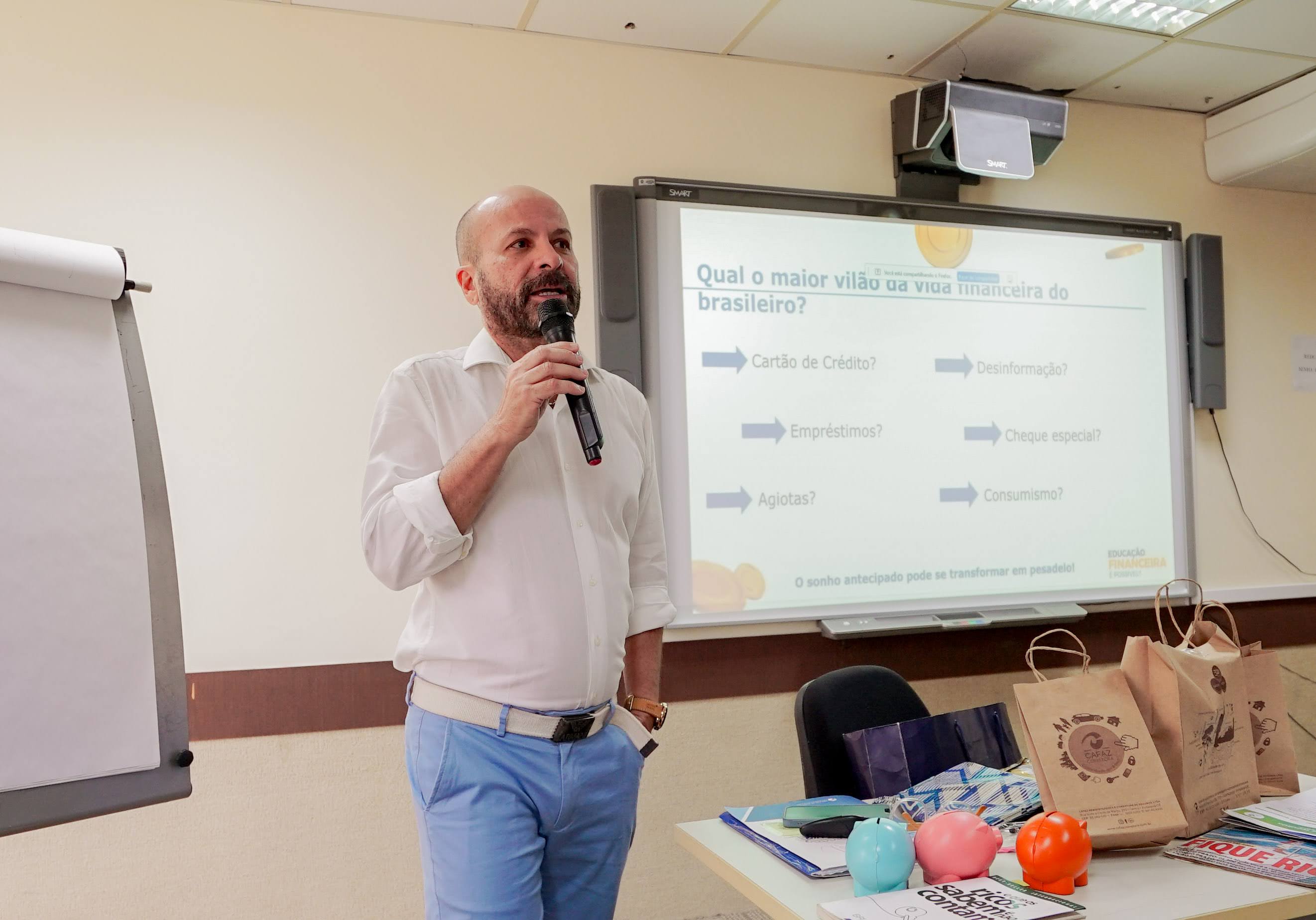 Foto do facilitador César Wagner. Ele está em pé, segurando o microfone e falando para os estagiários na sala de aula
