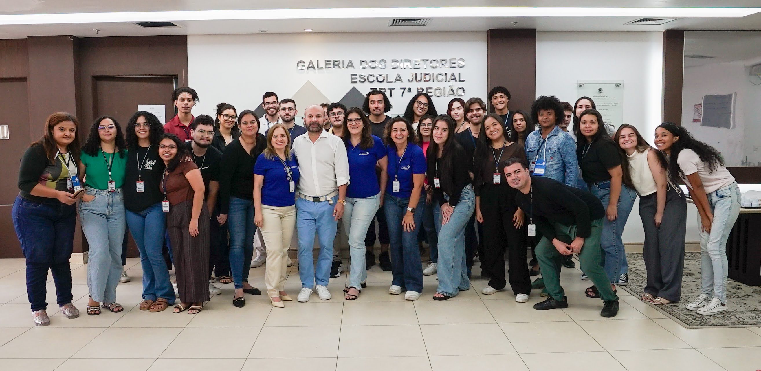 Foto de todos os estagiários junto com o educador financeiro César Wagner e três integrantes do subomitê gestor (Jamille, Ana Cláudia e Rejane). Eles estão em pé, juntos, em foto posada na parte do hall da Escola Judicial