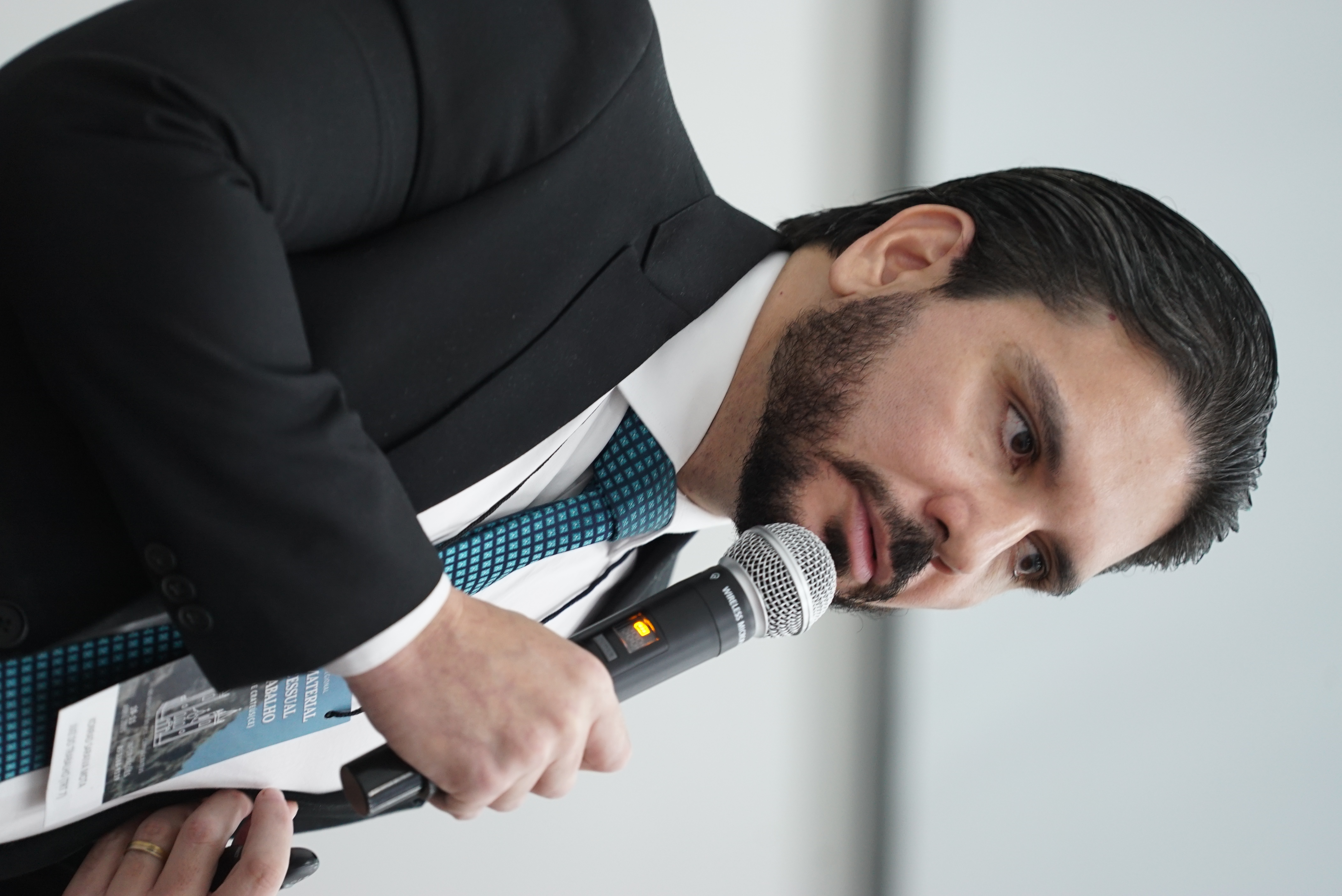 Foto do Konrad Saraiva Mota. Ele está falando ao microfone. O juiz usa paletó preto e gravata azul