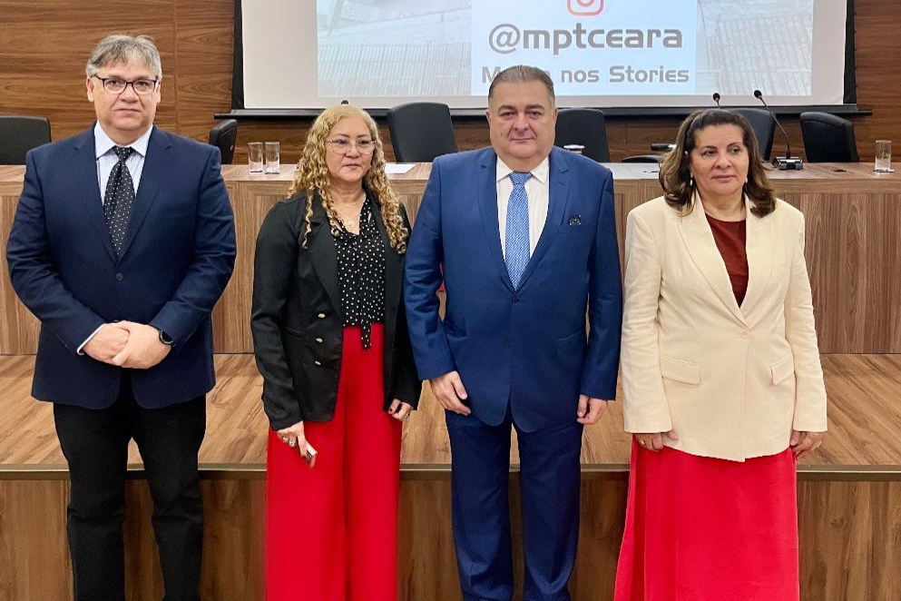  Duas mulheres e dois homens em pé na frente do palco com o logotipo do MPT no telão ao fundo