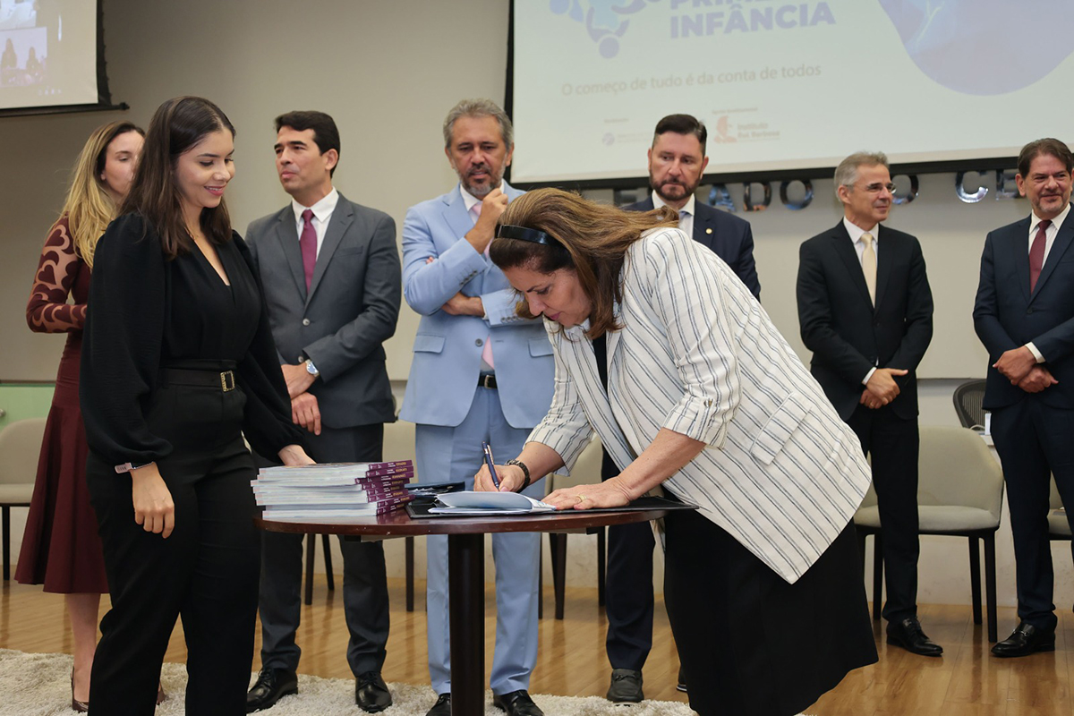 Desa. Fernanda assina um documento no palco com autoridades ao fundo