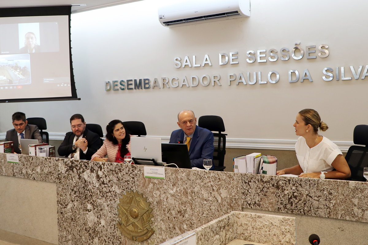 3 homens e 2 mulheres sentados na mesa de mármore da sala de sessões, com um brasão dourado na frente