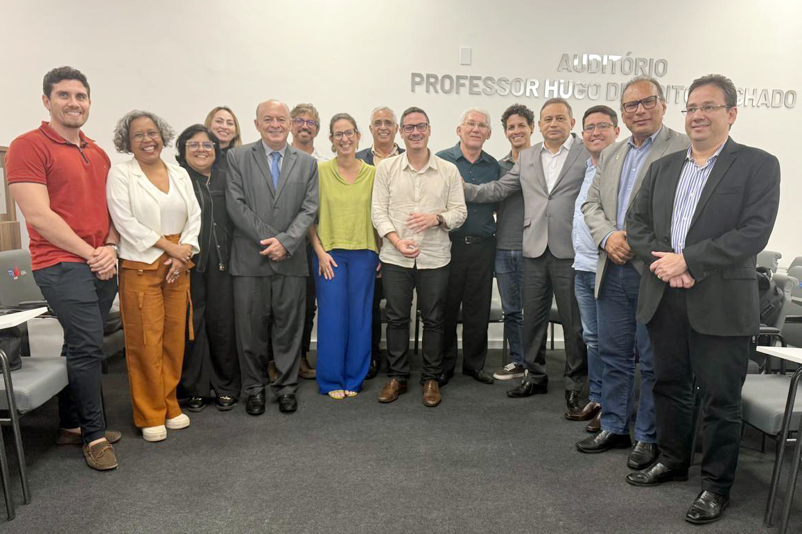 quinze pessoas em pé posam pra foto em sala de reunião