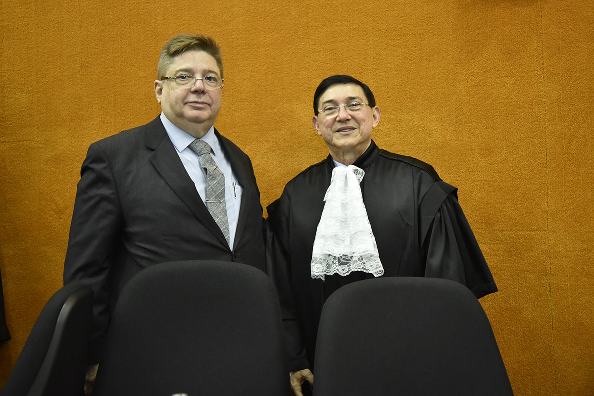 um homem de terno e gravata e outro homem de toga numa sala de paredes de madeira