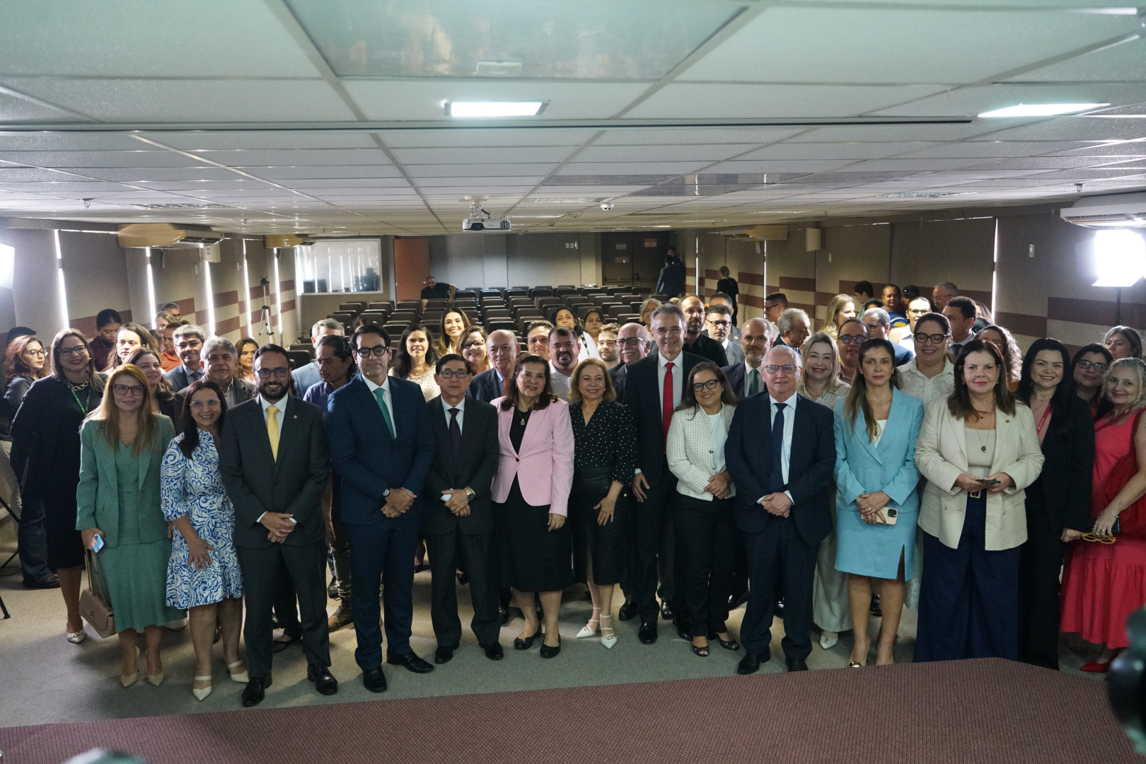 Foto posada com um grupo de aproximadamente 40 pessoas. Eles estão no auditório do TRT-CE e existem homens e mulheres com roupas formais.