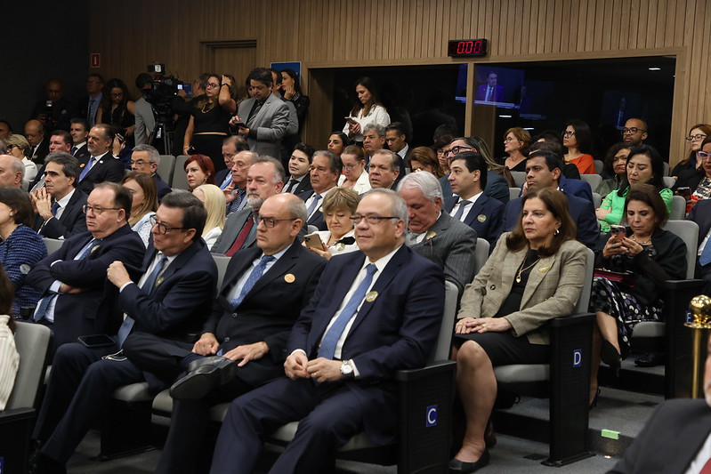  Nesta imagem, vemos um grupo de pessoas, aparentemente profissionais, sentadas em fileiras de assentos em um auditório. Muitos deles estão em trajes formais, como blazers e ternos, e alguns parecem estar prestando atenção a um evento ou apresentação.