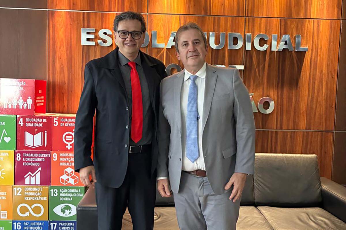 Um grande grupo de magistrados e palestrantes, em trajes sociais, sorri em uma foto de encerramento, de pé no auditório. No centro, o grupo da frente segura pastas e alguns buquês; ao fundo, é possível ver uma porta de saída de emergência.