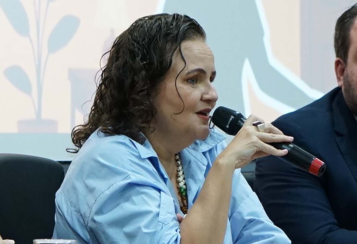 Quatro debatedores (três mulheres e um homem) sentados em uma mesa de madeira escura, de frente para uma plateia parcialmente visível em primeiro plano. Atrás, um telão exibe o título do seminário: "POR TRÁS DAS PORTAS: a invisibilidade do trabalho escravo doméstico".