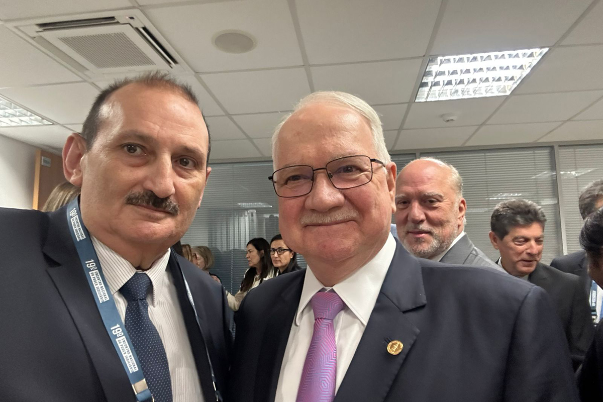  Uma foto em ambiente de evento mostra um grupo de cinco pessoas, todas com crachás, posando sob um painel que anuncia o 19º Encontro Nacional do Poder Judiciário em Florianópolis. O evento ocorreu de 1 a 2 de dezembro de 2025. A programação detalha painéis, palestras de ministros, e o 10º Fórum Nacional das Corregedorias (FONACOR) em 2 de dezembro, com Conferência dos Corregedores e encerramento.