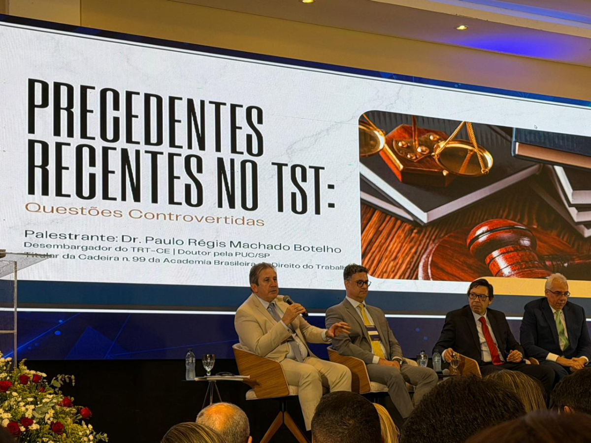 Desembargador Paulo Régis Machado Botelho, advogado Augusto Maranhão (presidente da mesa), professor Ricardo Guimarães e desembargador Sérgio Torres Teixeira compuseram a mesa do 1º painel. Todos estão sentados, de paletó e o des. Paulo Régis está falando ao microfone