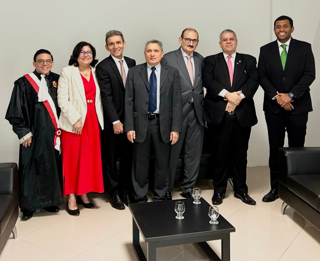 As imagens mostram o registro de uma cerimônia solene de premiação jurídica. O destaque é um homem de terno cinza e óculos que entrega uma medalha e um diploma ao Desembargador Francisco José Gomes da Silva, que veste beca preta com faixa vermelha e branca. Eles aparecem sorridentes em diferentes momentos, acompanhados por outros magistrados e convidados em um ambiente formal com bandeiras ao fundo.