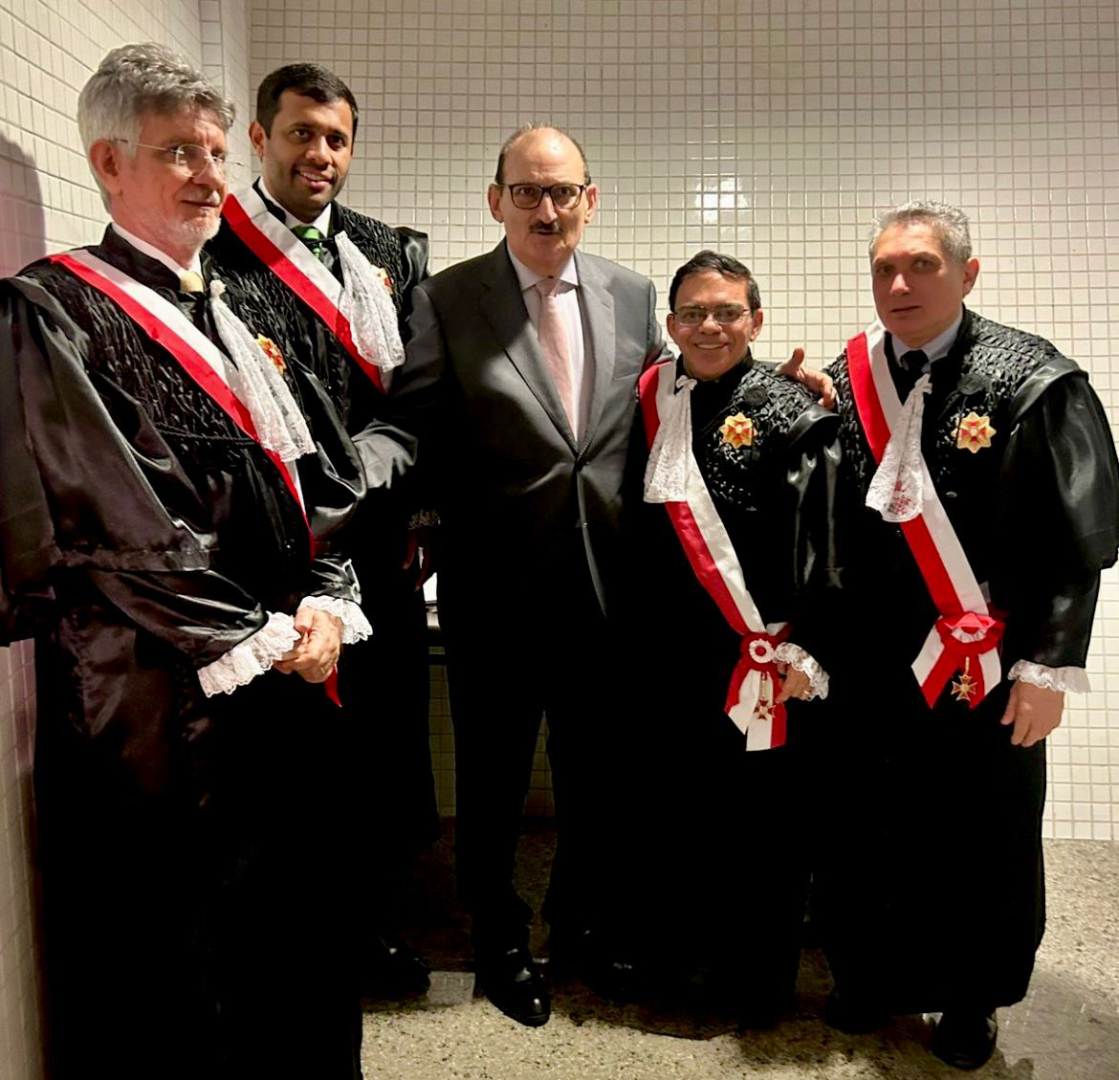 As imagens mostram o registro de uma cerimônia solene de premiação jurídica. O destaque é um homem de terno cinza e óculos que entrega uma medalha e um diploma ao Desembargador Francisco José Gomes da Silva, que veste beca preta com faixa vermelha e branca. Eles aparecem sorridentes em diferentes momentos, acompanhados por outros magistrados e convidados em um ambiente formal com bandeiras ao fundo.