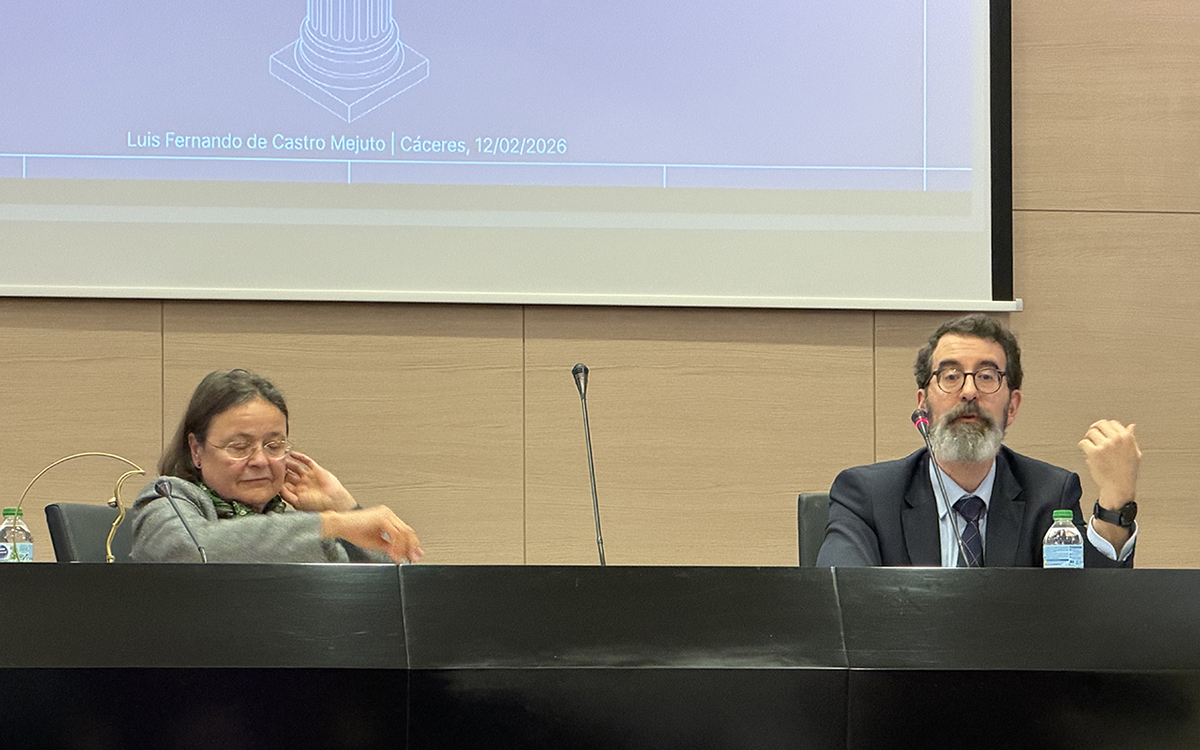 O palestrante Luis Fernando de Castro Mejuto, de terno escuro, barba grisalha e óculos, gesticula com a mão esquerda enquanto fala ao microfone em um painel sobre proteção de dados. À sua direita, uma colega de cabelos curtos e óculos observa a apresentação sentada à mesma bancada preta. Ao fundo, a parte inferior de um telão exibe o nome do palestrante e a data de 12/02/2026 em Cáceres.