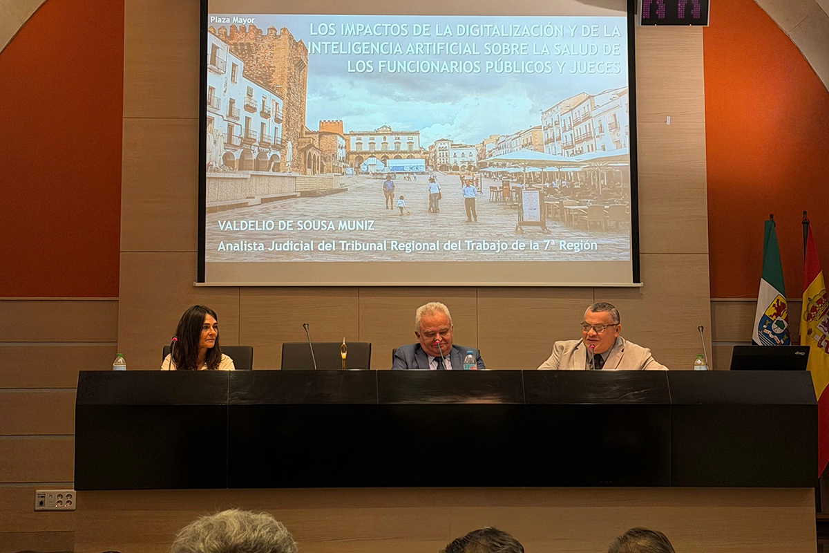 A fotografia oficial registra o encerramento do II Encuentro Hispano-Brasileño, com um grupo de aproximadamente 50 participantes posando de pé em um auditório de teto arqueado e iluminação suave. Os integrantes, vestidos com trajes formais e de inverno, ocupam a área central à frente de um telão que exibe o cartaz azul do evento, ladeado por painéis laterais em tom alaranjado vibrante. Em primeiro plano, as poltronas escuras do auditório aparecem em perspectiva, direcionando o olhar para a integração das delegações que sorriem para a câmera.