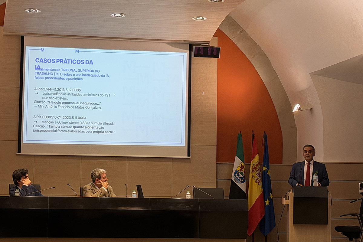 A fotografia oficial de encerramento reúne cerca de 50 participantes de pé no centro de um auditório com teto em arco e detalhes em laranja vibrante. O grupo, formado por homens e mulheres com roupas formais de inverno, sorri para a câmera à frente de um telão que exibe o cartaz azul do evento. Em primeiro plano, as poltronas escuras do auditório aparecem em perspectiva, completando a cena que simboliza a integração das delegações.